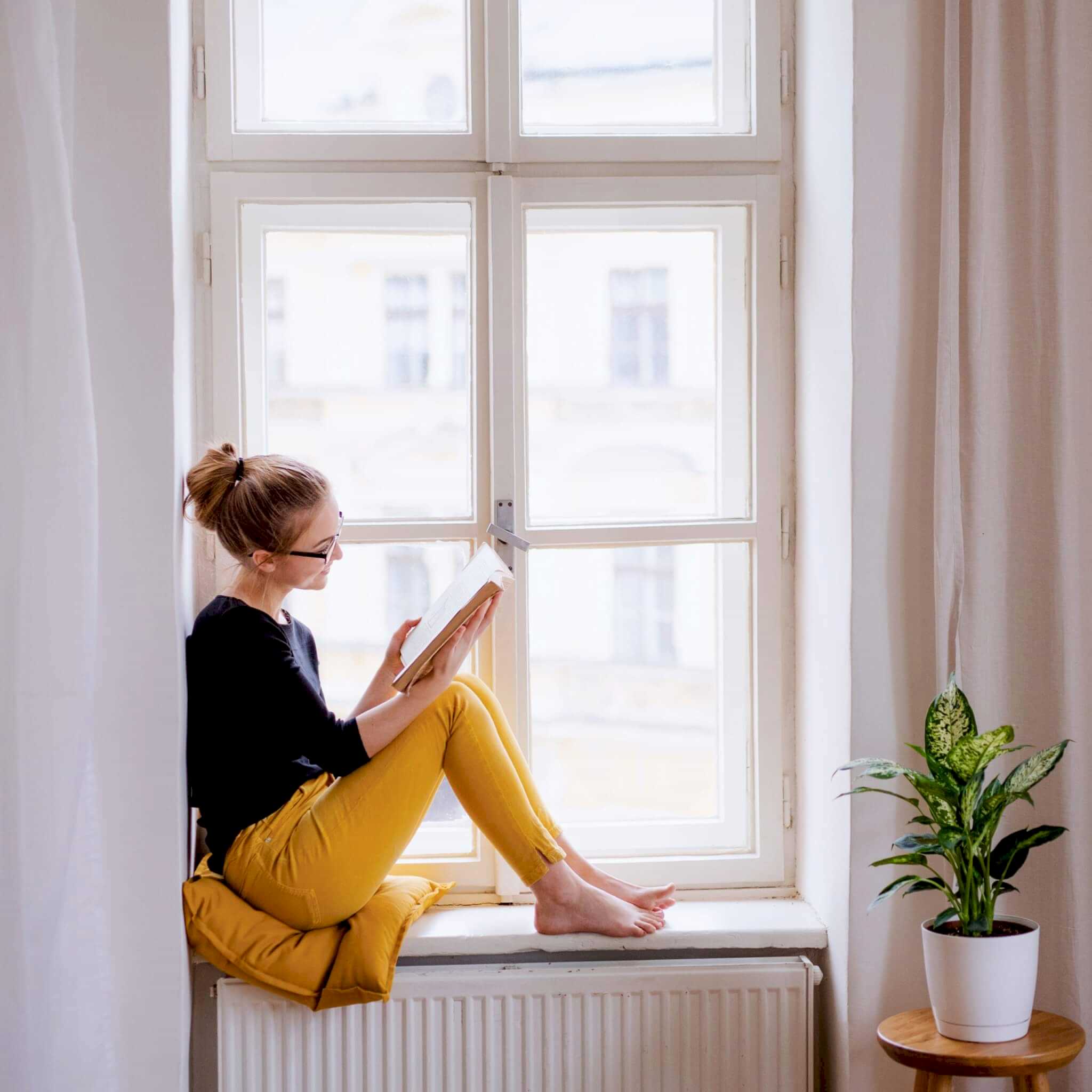 AdobeStock_272777633 young woman reading on the ledge of a window